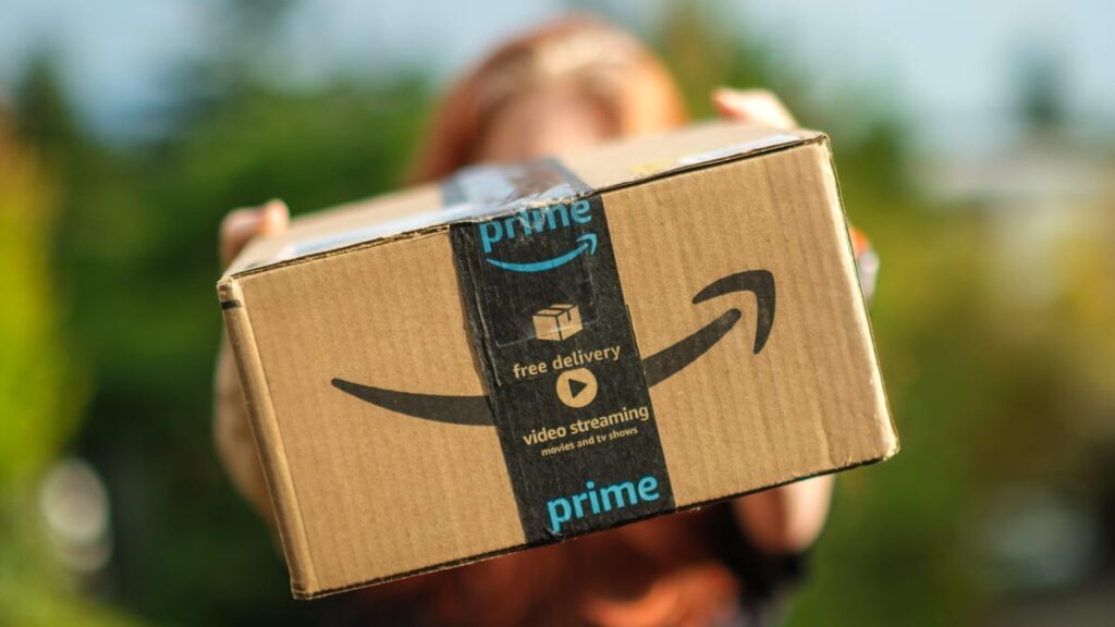 A person holds an Amazon cardboard shipping box toward the camera.